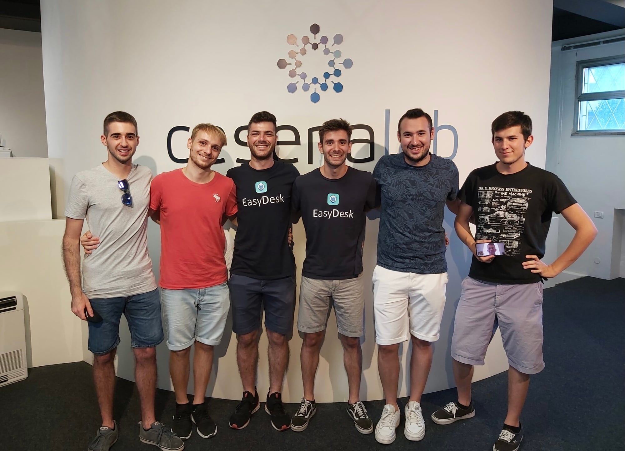 The EasyDesk team, six young founders and developers, smiling in front of the CesenaLab incubator sign, two of them in EasyDesk T-shirts